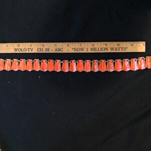 May include: A vintage orange and silver chain necklace with a repeating pattern of triangular shaped pendants. The necklace is approximately 8 inches long.