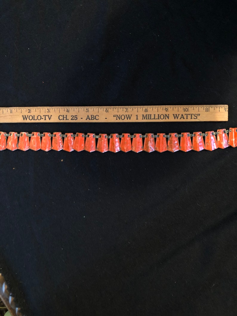 May include: A vintage orange and silver chain necklace with a repeating pattern of triangular shaped pendants. The necklace is approximately 8 inches long.