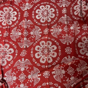 May include: A red woven throw blanket with a white pattern of eagles and stars. The blanket has a fringed edge.