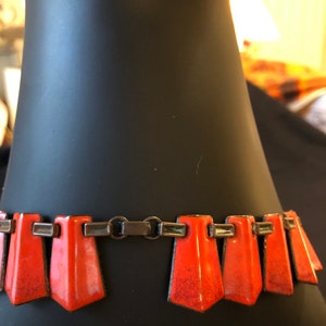 May include: A close-up of a vintage orange enamel and silver necklace. The necklace has a geometric design with a series of triangular pendants.