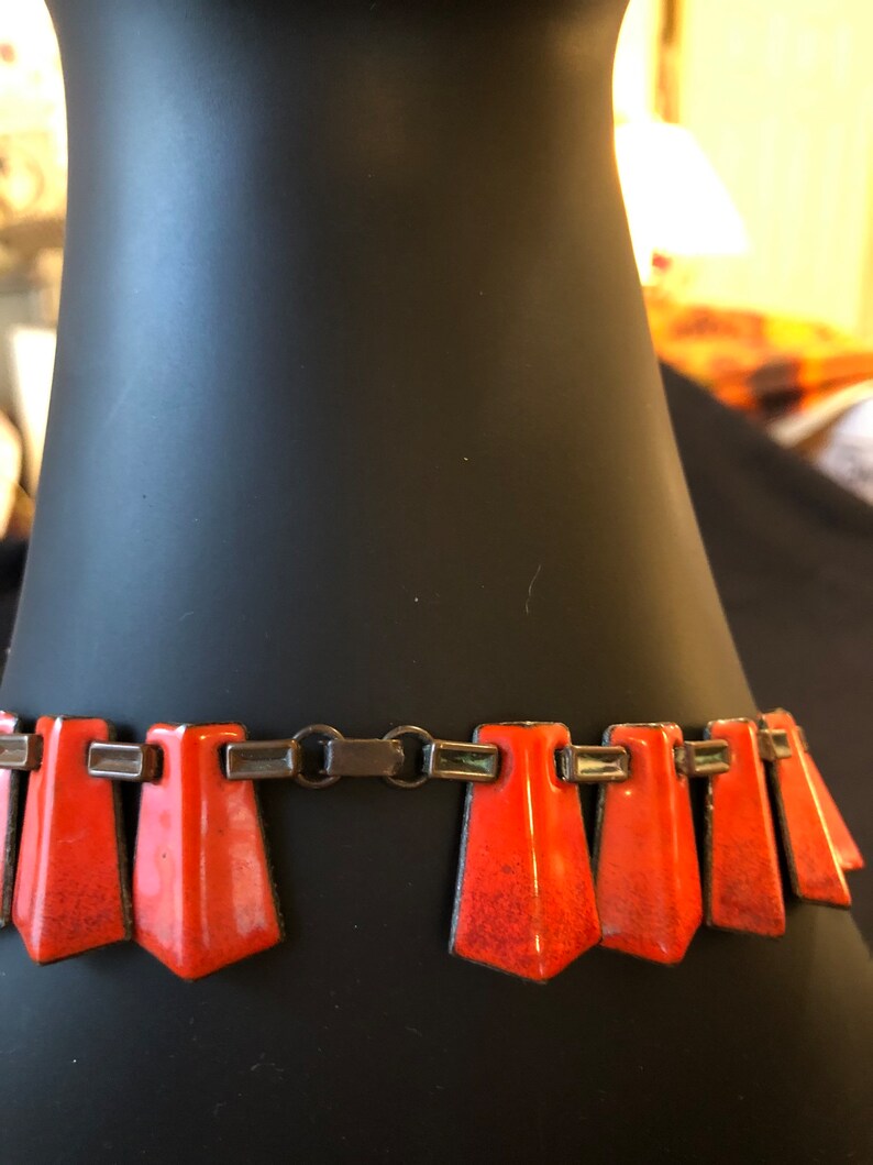 May include: A close-up of a vintage orange enamel and silver necklace. The necklace has a geometric design with a series of triangular pendants.