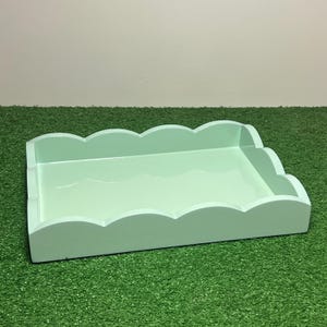 May include: A rectangular mint green tray featuring a smooth, glossy finish and raised scalloped edges on all four sides. The tray has a flat base and a consistent light green color throughout its entire structure, providing a simple, open surface.