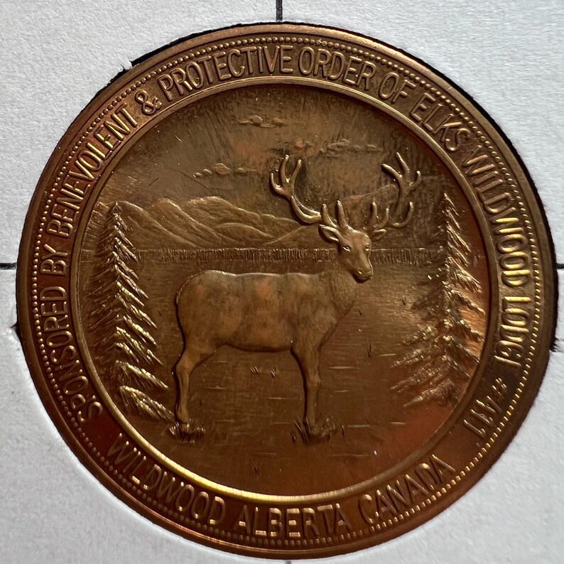 May include: A bronze-colored commemorative coin featuring a detailed depiction of a stag in a natural landscape. The coin's outer ring includes the text "Sponsored by Benevolent & Protective Order of Elks Wildwood Lodge #471 Wildwood Alberta Canada."
