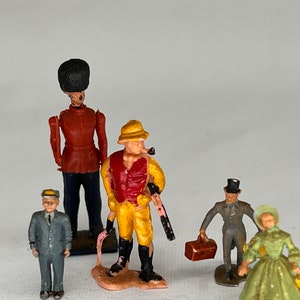 May include: A collection of vintage miniature figurines. The figures include a soldier in a red coat, a man in a yellow outfit with a pipe, a man in a suit, a man with a suitcase, and a woman in a green dress.