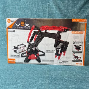 May include: A Hexbug Vex Robotics STEM Starter Kit box. The box features a robotic arm with red and black components, a control box, and the text "Pick Up Motorized Claw". The box also shows two alternate builds: a chopper and a scorpion.