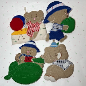 May include: A collection of whimsical fabric appliques featuring animal characters. Each applique depicts a different animal, such as a bear, elephant, and beaver, wearing hats and holding various items like a watermelon and apple. The appliques are in shades of brown, blue, red, and green.