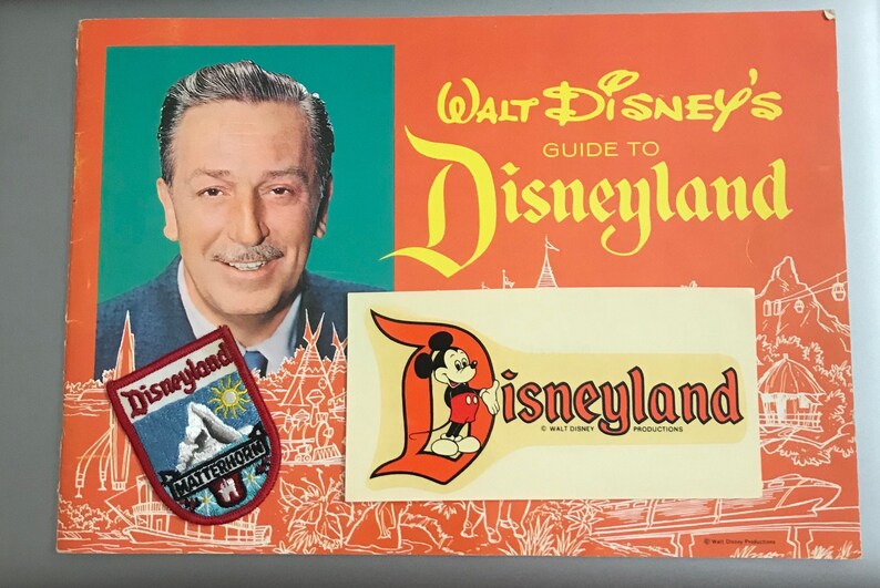 Puede incluir: Una gu&iacute;a vintage de Disneyland con un parche de Disneyland rojo, blanco y azul, una pegatina de Disneyland amarilla y blanca y una foto de Walt Disney.