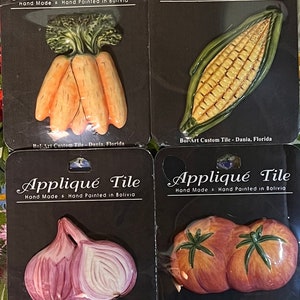 May include: Four ceramic tile appliques featuring hand-painted vegetables. The tiles are packaged on individual cards with the text "Appliqué Tile Hand Made & Hand Painted in Bolivia Bol-Art Custom Tile - Dania, Florida". The vegetables are carrots, corn, onions, and tomatoes.