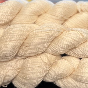 May include: A close-up of a skein of off-white yarn. The yarn is soft and fluffy, and it is perfect for knitting or crocheting.