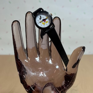 May include: A black wristwatch with a white face featuring a Mickey Mouse design. The watch has a black leather band and a gold-colored crown. The watch is a classic and fun accessory.