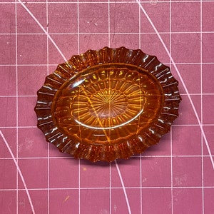 May include: A small, amber-colored glass dish with a scalloped edge and a raised, patterned design in the center.