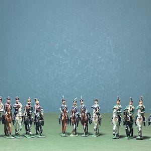 May include: A collection of miniature toy soldiers on horseback, painted in various uniforms with detailed features. The figures are arranged on a green surface against a blue-green backdrop, showcasing historical military attire.