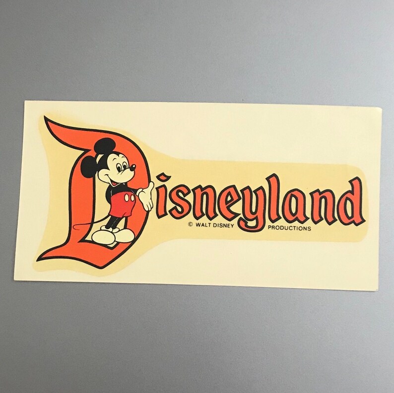 Puede incluir: Pegatina vintage de Disneyland con Mickey Mouse con un atuendo rojo y negro, de pie frente a una "D" naranja estilizada con la palabra "Disneyland" en letras naranjas. La pegatina incluye la informaci&oacute;n de copyright "&copy; WALT DISNEY PRODUCTIONS".