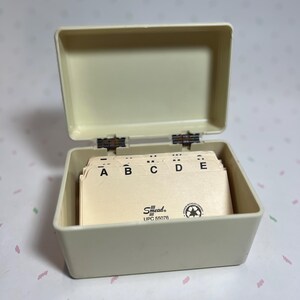 May include: An open, off-white address card box with a hinged lid. The box contains a stack of cream-colored index cards labeled A, B, C, D, and E. The brand name "Smead" is visible on the cards.