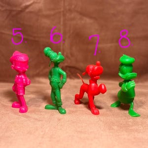 May include: Five vintage plastic cartoon character figurines. The figurines are green and red. The characters are Peter Pan, Goofy, Pluto, and Donald Duck.