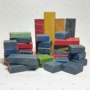 May include: A collection of colorful wooden blocks in various shapes and sizes. The blocks are painted in shades of blue, green, red, and yellow. Some blocks are rectangular, while others are square. The blocks are arranged in a playful, stacked configuration.