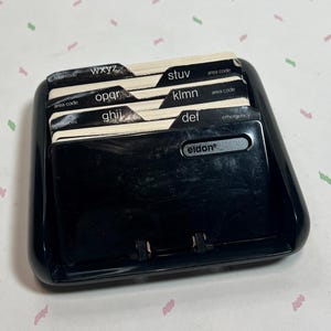 May include: A black plastic address book with labeled dividers. The dividers are labeled with letters of the alphabet and include the brand name "Eldon". The address book is designed to hold contact information.
