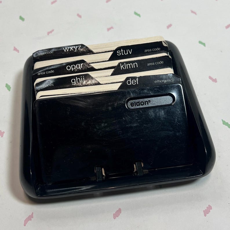 May include: A black plastic address book with labeled dividers. The dividers are labeled with letters of the alphabet and include the brand name "Eldon". The address book is designed to hold contact information.