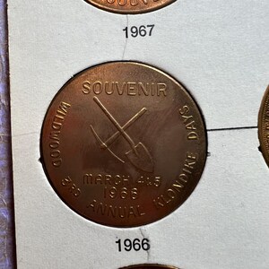 May include: A copper-colored souvenir coin from the 3rd Annual Wildwood Klondike Days, dated March 4 & 5, 1966. The coin features a crossed pickaxe and shovel design, with the word "SOUVENIR" at the top.