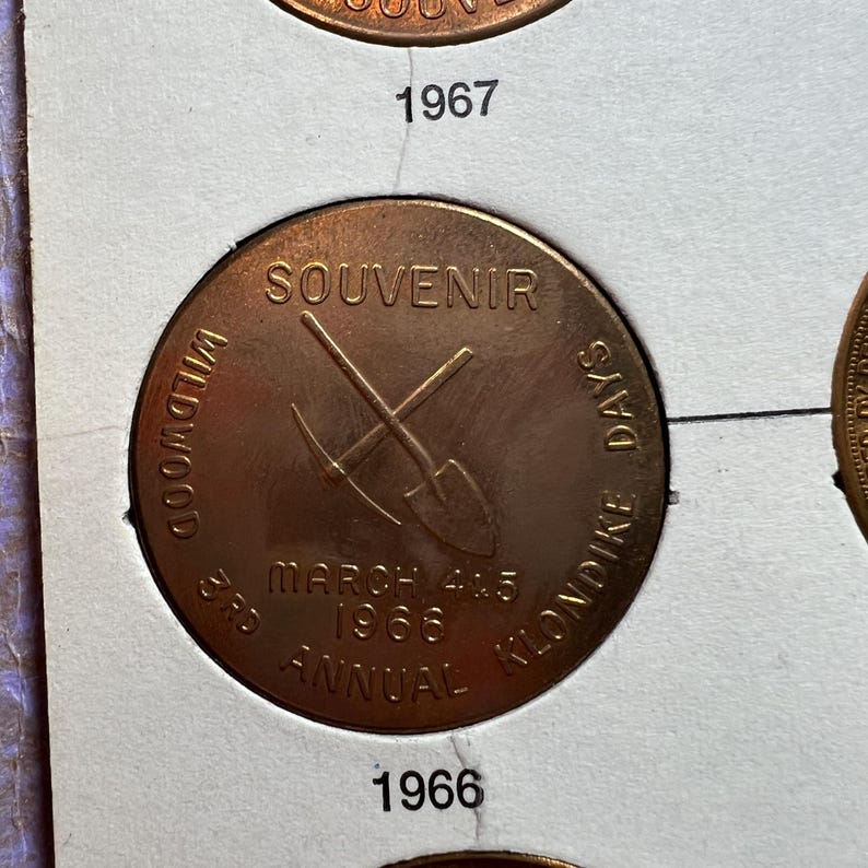 May include: A copper-colored souvenir coin from the 3rd Annual Wildwood Klondike Days, dated March 4 & 5, 1966. The coin features a crossed pickaxe and shovel design, with the word "SOUVENIR" at the top.