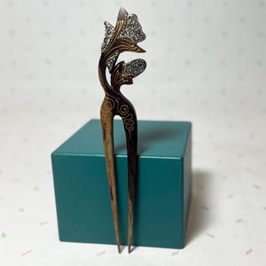 May include: A wooden hair fork with a decorative butterfly design. The hair accessory features intricate carvings and silver accents. The fork is dark brown with lighter wood tones and is displayed on a teal box.