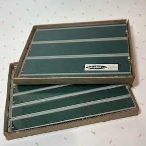 May include: Two rectangular, dark green panels with silver stripes and a clear cover, stacked in cardboard boxes. The panels have the text "mioplex" and "multiple strip contact" on a white label.