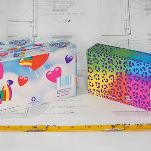 May include: Two rectangular cardboard boxes with a yellow measuring tape showing a length of 17 inches. One box features a blue sky background with colorful hearts and the text This Box Belongs To. The other box has a rainbow leopard print pattern.
