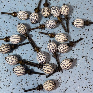 May include: A collection of white and blue ceramic cabinet knobs with a dotted and striped design. The knobs have a brass-colored base and a threaded rod for installation. The knobs are scattered on a light blue surface.
