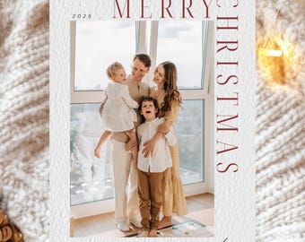 May include: A white Christmas card with the words "MERRY CHRISTMAS" in burgundy. The card features a family portrait with the year 2025 and the family name in script. The card is set against a textured white background.