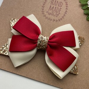 May include: A red and white bow with gold glitter accents. The bow is handmade and has a "Hand Made with Love" stamp on the background.