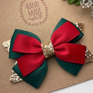 May include: A red and green bow with gold glitter accents. The bow is handmade and has a "Hand Made with Love" stamp on the background.