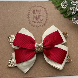 May include: A red and white bow with gold glitter accents. The bow is handmade and has a "Hand Made with &hearts;" stamp on the background.