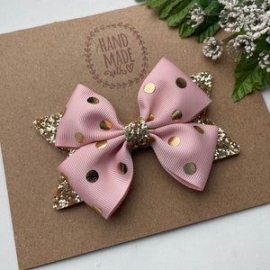 Peut inclure: Un n&oelig;ud rose et or &agrave; pois avec des accents de paillettes. Le n&oelig;ud est fait &agrave; la main et porte un tampon "Hand Made with Love" sur le fond.