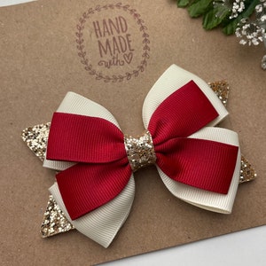 May include: A red and white ribbon bow with gold glitter accents. The bow is handmade and has a "HAND MADE with &hearts;" stamp on the background.