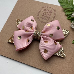 Peut inclure: Un n&oelig;ud rose et or &agrave; pois avec des accents de paillettes. Le n&oelig;ud est fait &agrave; la main et porte une &eacute;tiquette qui dit "Hand Made with love".