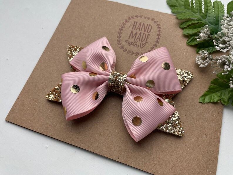Peut inclure: Un n&oelig;ud rose et or &agrave; pois avec des accents de paillettes. Le n&oelig;ud est fait &agrave; la main et porte une &eacute;tiquette qui dit "Hand Made with love".