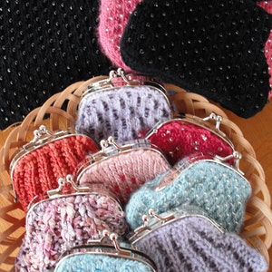 May include: A collection of knitted coin purses in a variety of colors and patterns, including black, pink, blue, and purple. The purses are arranged in a wicker basket.