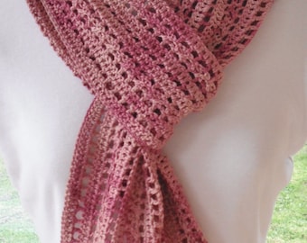May include: A crocheted scarf in shades of pink and red with a lacy pattern. The scarf is draped over a white mannequin.