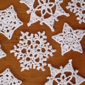 May include: A collection of eight white crocheted snowflakes, each with a unique design, displayed on a wooden surface.