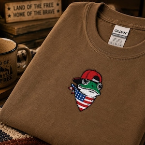 Camiseta patriótica de rana: Pañuelo con la bandera estadounidense y gorra roja para la celebración del 4 de julio.