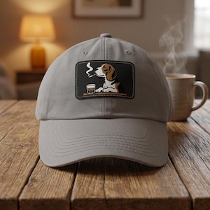 May include: A light grey baseball cap featuring a rectangular patch on the front. The patch displays a graphic illustration of a beagle dog with a cigar in its mouth and a glass of amber liquid on a table, with white smoke rising from the cigar.