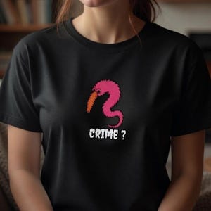 May include: Black t-shirt featuring a pink worm-like creature with an orange beak. The text "CRIME ?" is printed in white below the graphic. The shirt is a short-sleeved crew neck.
