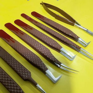 Puede incluir: Un conjunto de pinzas marrones y plateadas con mangos texturizados y puntas anguladas, dispuestas sobre una superficie amarilla brillante. El texto "Beauty HubSpcial" es visible en la esquina superior izquierda.