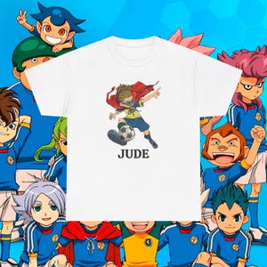 May include: White t-shirt with a cartoon image of a soccer player wearing a red cape, with the name "JUDE" below. Other cartoon characters in blue uniforms surround the shirt.