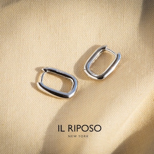 May include: Two silver-colored, oval-shaped hoop earrings. The earrings are displayed on a beige fabric. The brand name "IL RIPOSO NEW YORK" is printed in black at the bottom of the image.