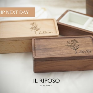Puede incluir: Dos cajas rectangulares de madera, una clara y otra oscura, con grabados florales y nombres personalizados. La caja clara est&aacute; grabada con "Lillian", y la oscura con "Bella".
