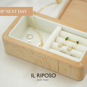Puede incluir: Caja de joyer&iacute;a de madera con interior blanco, que contiene varios pendientes, anillos y un collar. Los pendientes son de oro y plata con piedras preciosas y perlas. La caja tiene el texto "IL RIPOSO NEW YORK".