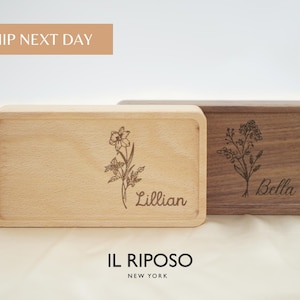 Puede incluir: Dos cajas rectangulares de madera, una clara y otra oscura, con grabados florales y nombres. La caja clara tiene "Lillian" y la oscura "Bella". El texto "SHIP NEXT DAY" est&aacute; arriba y "IL RIPOSO NEW YORK" abajo.