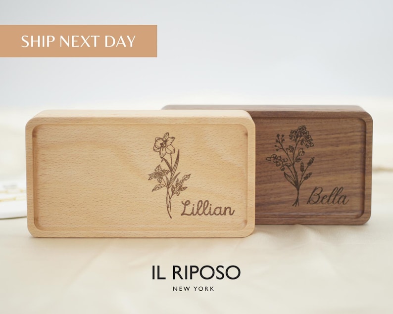 Puede incluir: Dos cajas rectangulares de madera, una clara y otra oscura, con grabados florales y nombres. La caja clara tiene "Lillian" y la oscura "Bella". El texto "SHIP NEXT DAY" est&aacute; arriba y "IL RIPOSO NEW YORK" abajo.