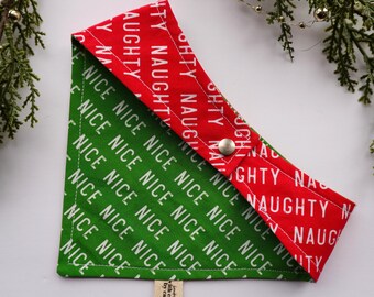 May include: A festive dog bandana with a red and green design. The red section is printed with the word "NAUGHTY" in white, while the green section features "NICE". A metal snap closure secures the bandana. A small tag reads "with care. by care."